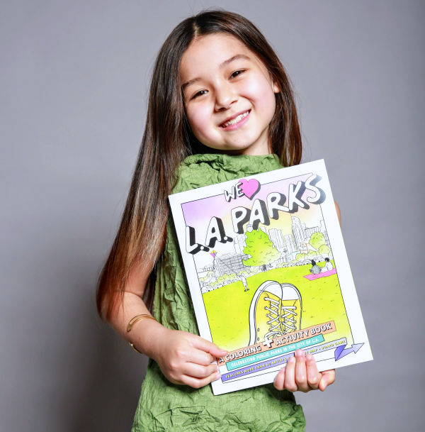 Girl with long brown hair holding a coloring book against gray background
