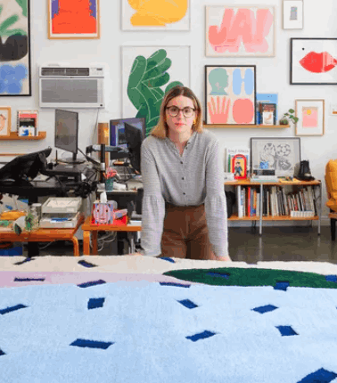 Woman with glasses with large patterned rug in front of her.